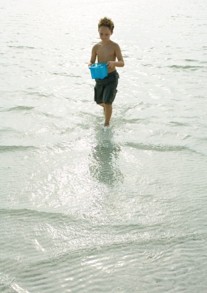 boy walking through surf with bucket
