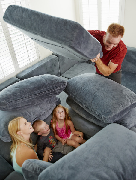 father covering family sitting among cushions