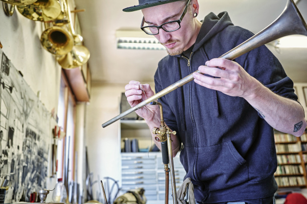instrument maker making trumpet in workshop