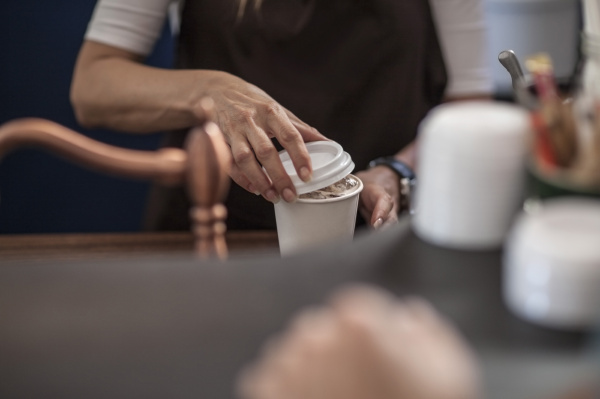 barista closing lid of disposable coffee