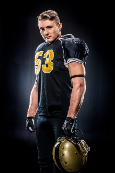 Beautiful female american football player in sportswear and helmet holding  ball on black Stock Photo by LightFieldStudios