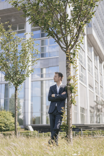 businessman leaning against a tree in