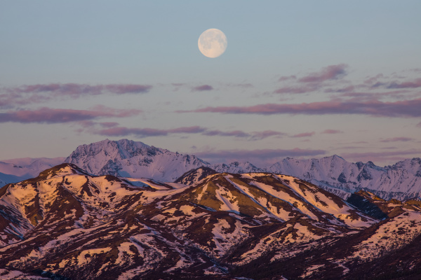 the moon rises over the mountains