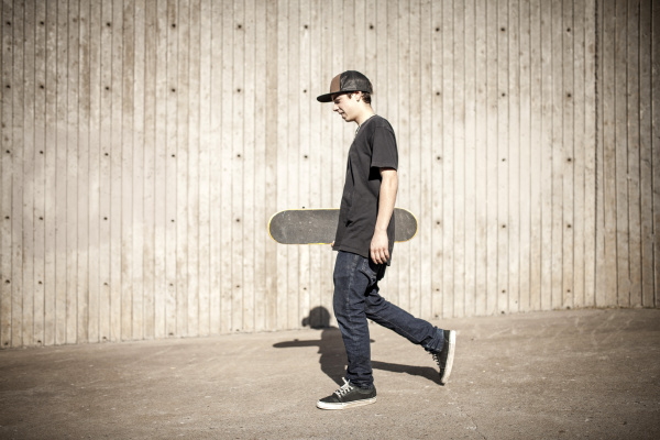 caucasian man carrying skateboard near wooden
