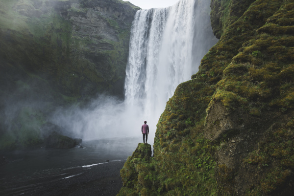 man standing by skogafoss waterfall in