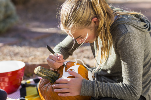 a teenage girl carving pumpkin outdoors