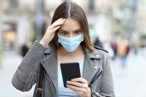 worried woman with mask checking phone