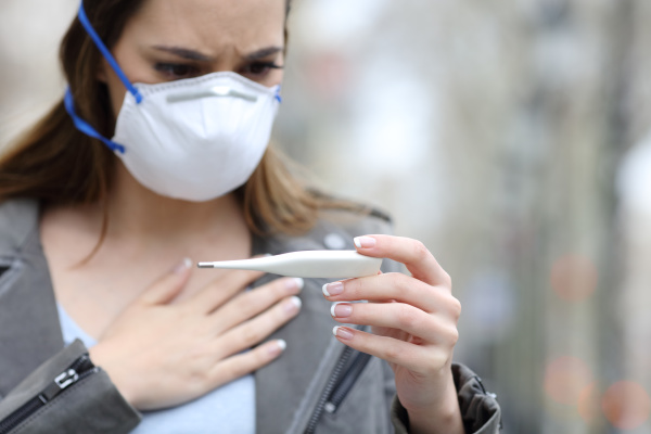 woman with protective mask checking thermometer