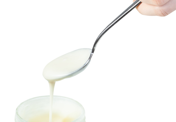 white honey pouring from steel spoon