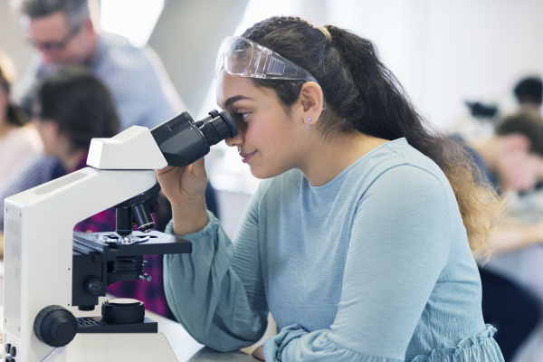 girl student using microscope conducting