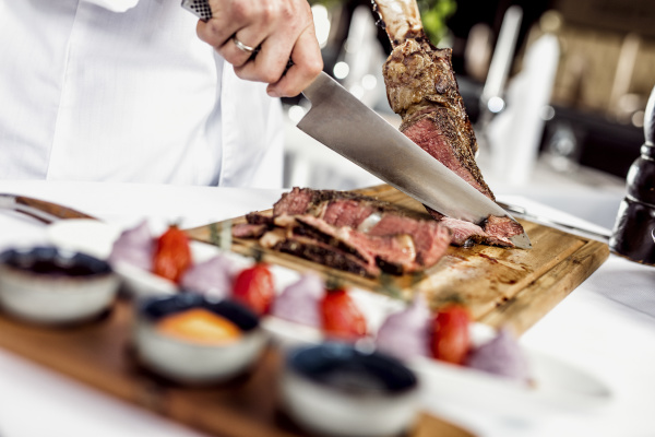 hands of chef slicing tomahawk steak