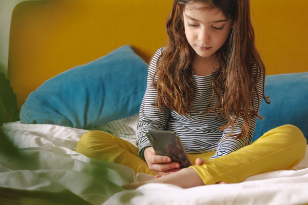 girl using smartphone sitting on bed