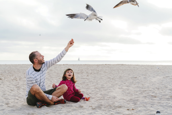 father feeding seagulls while sitting with