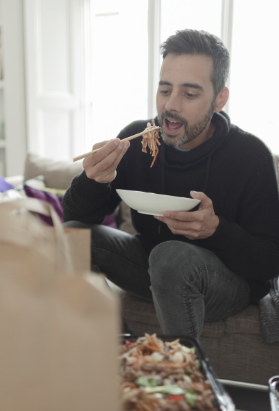 man eating takeout noodles with chopsticks