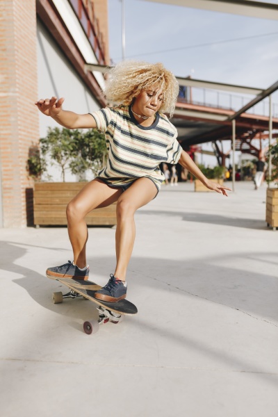 blond woman with arms outstretched skateboarding