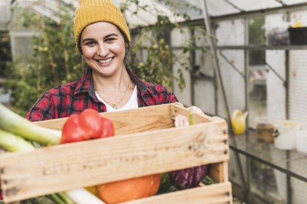 smiling woman carrying crate with vegetables