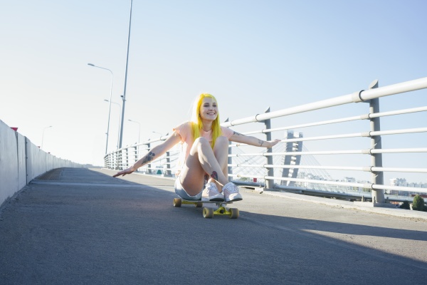 young woman sitting on skateboard against