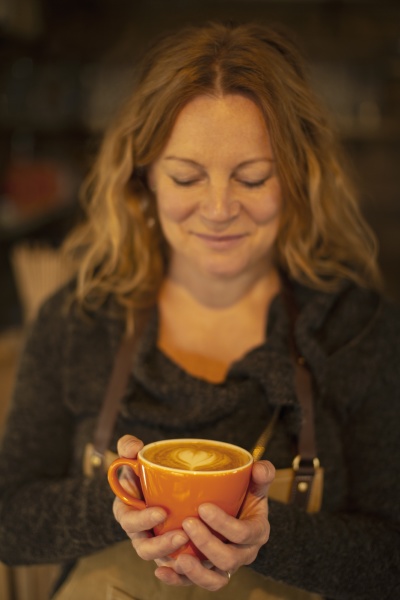 happy female barista holding cappuccino with