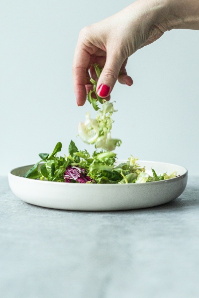 hands putting ingredients in a salad
