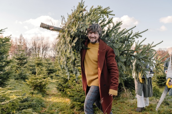 man carrying christmas tree on shoulder